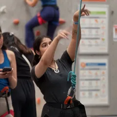 A climber manages the rope for her partner, demonstrating the teamwork and trust that is central to the sport.