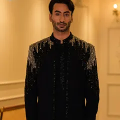 A full-length portrait in a striking black Indo-Western tuxedo. The cascading silver and black beadwork on the shoulders creates a dramatic and glamorous effect, perfect for a grand reception.