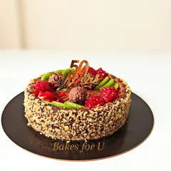 A whole wheat cake created for a 50th anniversary celebration. The sides are coated in chopped nuts, and the top is decorated with fresh raspberries, kiwi, and Ferrero Rocher chocolates.