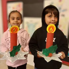 The joy of the season shines through as these two young artists show off their completed Christmas candle holders, complete with paper flames and holly leaves.