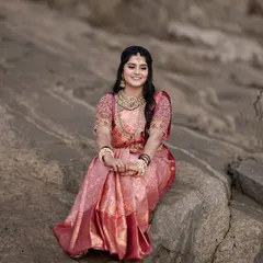 A beautiful bridal portrait of the bride seated on a rock. Her joyful smile and stunning pink saree stand out against the natural, rugged background.