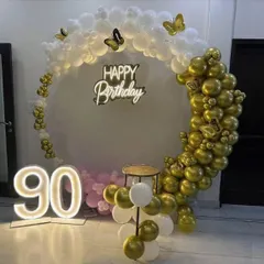 Celebrating a 90th birthday in style with this gold and white balloon arch. The setup includes large light-up numbers and butterfly accents for a graceful touch.