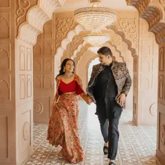 A happy, candid moment as an expecting couple walks hand-in-hand through an ornate, traditional Indian corridor. Their coordinated Indo-western outfits add a touch of cultural elegance to this natural, in-motion maternity photograph.