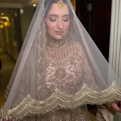 A beautiful shot of the bride under her veil. The soft, diffused lighting highlights the golden hues of her outfit and the luminous quality of her skin, creating a timeless and elegant bridal portrait.
