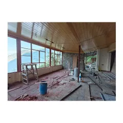 The interior of the homestay extension nearing completion. The warm wood-paneled ceiling and large windows create a cozy and inviting atmosphere, perfect for enjoying the mountain views.