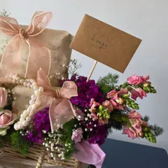 A closer look at the details, showing a handwritten note and the interplay of textures between the rustic wicker basket, soft ribbons, and delicate flowers.
