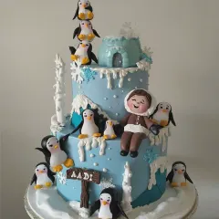 A winter wonderland adventure for a special birthday boy. This two-tiered cake is covered in snowy details, a fondant igloo, and a whole colony of adorable, hand-sculpted penguins. The personalized figurine of the birthday boy makes him the star of this chilly, charming scene.