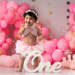 A playful and adorable moment from a first birthday shoot. Her cheeky expression and the beautifully decorated set create a picture-perfect memory of this special day.