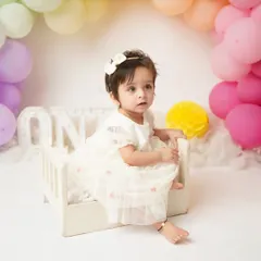 A thoughtful expression from the birthday girl, sitting in her miniature bed. Milestone sessions capture the full range of your child's adorable expressions.