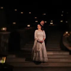 A majestic night portrait on the steps of a palace in Udaipur. The ambient lighting creates a dreamy, cinematic atmosphere, highlighting the bride's stunning lehenga.