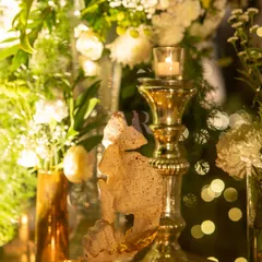 A close-up of a gold candelabra and a small sculpture, surrounded by white flowers and the soft bokeh of fairy lights. This is how I layer light and texture to create depth and romance.