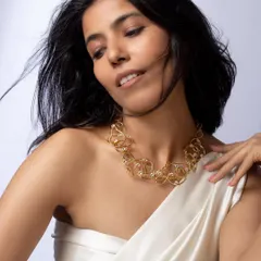A studio portrait modeling a bold, gold-toned abstract necklace, with a focus on how the piece sits on the collarbone.