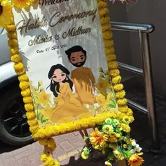 A personalized welcome easel for a Haldi ceremony, featuring a cute caricature of the couple and decorated with marigold flowers.