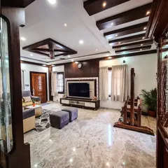 I designed this expansive living room to feel both grand and inviting, featuring Italian marble flooring and a complex coffered ceiling with both wood beams and recessed lighting. The space is anchored by a large, modern TV unit and includes a traditional wooden jhoola (swing), blending contemporary luxury with classic Indian elements.