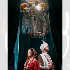 The bride and groom standing back-to-back under a magnificent chandelier after their wedding ceremony. This stylish portrait captures their stunning traditional attire and the opulence of the wedding decor.