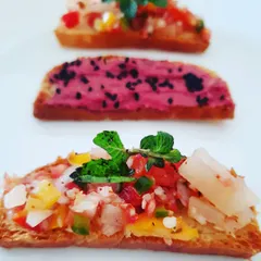 An assortment of gluten-free crostini with exciting toppings. One features a bright pink beetroot hummus, while the other is topped with a fresh and tangy pineapple salsa.