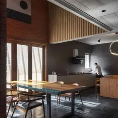 The kitchen and dining area in the Brick House, where a double-height ceiling and large doors create an airy, light-filled space. The material palette of brick, wood, and dark stone is honest and tactile.
