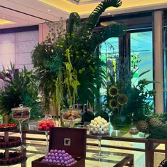Here, the focus is on the interplay between the organic floral art and the refined desserts. The large green installation, featuring sunflowers and curled leaves, perfectly frames the neatly arranged sweets, creating a luxurious and inviting display.