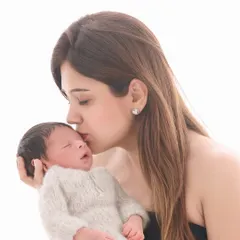 A mother gently kisses her sleeping baby's forehead in a simple, high-key portrait that emphasizes the pure and simple love between them.