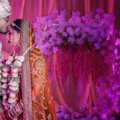 An intimate moment between the bride and groom, with the groom placing a gentle kiss on her forehead. The soft purple lighting creates a romantic and dreamy atmosphere for this classic wedding portrait.