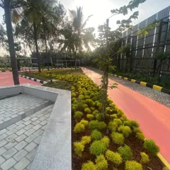 A vibrant red jogging path at Vaishnavi Tech Square is lined with neatly arranged shrubs and young trees. This demonstrates our approach to combining functional elements for fitness with organized, aesthetic planting.