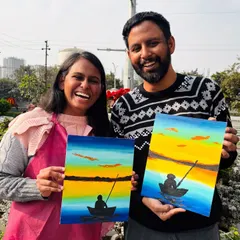 A couple showing off their matching sunset-over-the-water paintings. A perfect result from a relaxing and romantic paint date.