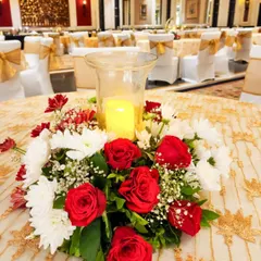 A classic and elegant table centerpiece with a candle in a glass hurricane lamp, surrounded by a wreath of red and white roses and chrysanthemums.