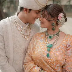A tender close-up of the couple, highlighting the bride's stunning emerald jewelry and the groom's classic sherwani.