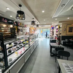 A wide view of our bakery interior, showing the long display counter filled with cakes, pastries, and savory items, with our cozy seating area in the background.