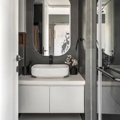 A sophisticated bathroom with a monochrome palette of black and grey. The floating white vanity and oval mirror create a clean, minimalist look, while the dark tiles add a sense of drama.