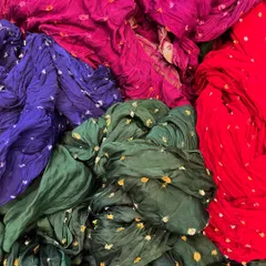 A vibrant pile of bandhani fabrics showing local shade samples of organic dyes. I explore these traditional techniques to offer a wide range of authentic colors, including deep greens, reds, and purples.