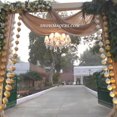 The entrance to the Soven & Valeria Roka ceremony, where a stunning chandelier hangs beneath draped fabric, framed by garlands of white and gold spheres.