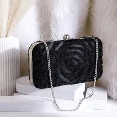 A sophisticated shot of a black beaded clutch bag, placed on a white pedestal against a soft, fluffy background to emphasize its texture and elegance.
