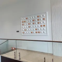 An angled view of the symmetrical relief sculpture. This perspective highlights how the artwork occupies the space and complements the surrounding architectural elements like the glass railing and textured wall panel.
