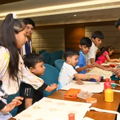 I am seen here guiding a young boy during a tote bag painting session, while other children work on their own creations. I provide gentle encouragement and help to ensure every child feels proud of what they make.