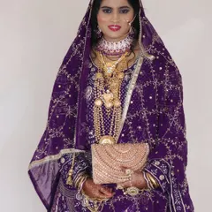 A stunning reception look for a Muslim bride. She is wearing a rich purple outfit with intricate gold embroidery, and her makeup is kept elegant to balance the ornate dress.