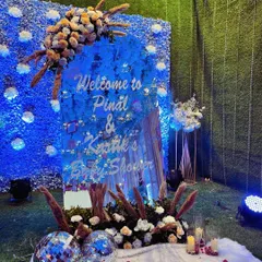 A custom acrylic welcome sign for a baby shower, set against a vibrant blue flower wall. The sign is adorned with pampas grass and floral arrangements, with disco balls at the base to add a touch of sparkle and fun.