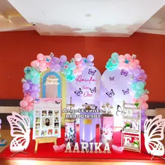 An enchanting butterfly theme in pastel shades of purple, pink, and mint green. The decoration features two arched backdrops, a full balloon garland, custom name lettering, and whimsical butterfly wing props for a magical party atmosphere.