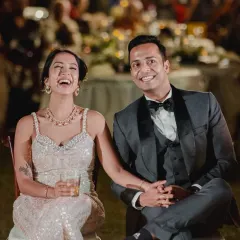 The bride and groom share a laugh while seated at their reception, enjoying the speeches and the company of their loved ones.