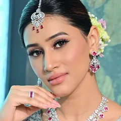 A perfect example of modern bridal glam where less is truly more. This close-up focuses on the flawless, skin-like foundation, soft pink lips, and clean eyeliner. The makeup enhances her features beautifully, complementing the diamond and ruby jewelry for a fresh, elegant reception look.