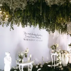 A quiet corner within the grand entrance, featuring a romantic quote, elegant white furniture, and classical statuary, all under a canopy of hanging foliage and crystals.