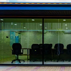 A view into the glass-walled conference room at the Prestige container office. The design emphasizes transparency and openness, connecting the indoor workspace with the surrounding landscaped environment.