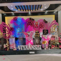 An elaborate stage setup for a butterfly-themed birthday party. This grand design features large pink butterfly wing cutouts, balloon garlands, custom-lit name signs, and themed pedestals for the cake, transforming the venue into a fairytale setting.