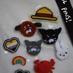 A collection of some of my most popular pin designs on a tote bag. You can see pride hearts, animals, and even a straw hat from One Piece.