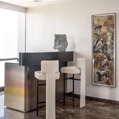 This bar area is treated as a single, monolithic piece with an ombre metallic finish. To keep the focus on the bar itself, we designed sleek, high-backed bar stools in a contrasting black and white.