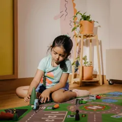 In our Makerspace, children have the freedom to explore independently. Here, a child is engrossed in creating her own world with a city-themed play mat and wooden toys.