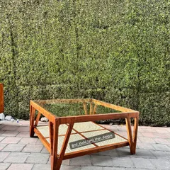A custom-made square coffee table with a glass top, teak frame, and a distinctive cane lower shelf.
