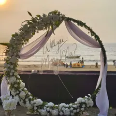 A closer look at the romantic proposal arch. The transparent 'Will you Marry Me?' sign allows the beautiful beach sunset to shine through, while the lush white floral arrangement creates an elegant and timeless frame for the big moment.