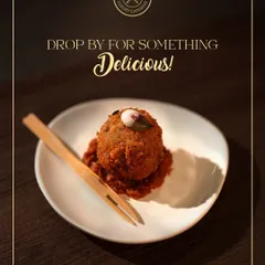 A single, perfectly crafted appetizer, possibly a modern take on a kebab or croquette, served on a bed of rich sauce. This image represents our philosophy: luxury served in every bite.
