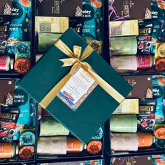Celebrate in style with our elegant festive hampers. This custom Diwali gift for South Western Railways features a deep green box tied with a gold ribbon and a personalized "Happy Diwali" tag, surrounding a curated selection of treats.